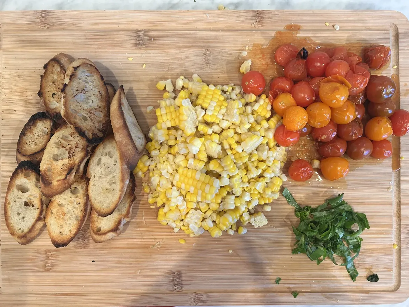 Crostini, blistered cherry tomatoes and sweet corn prepped on a cutting board
